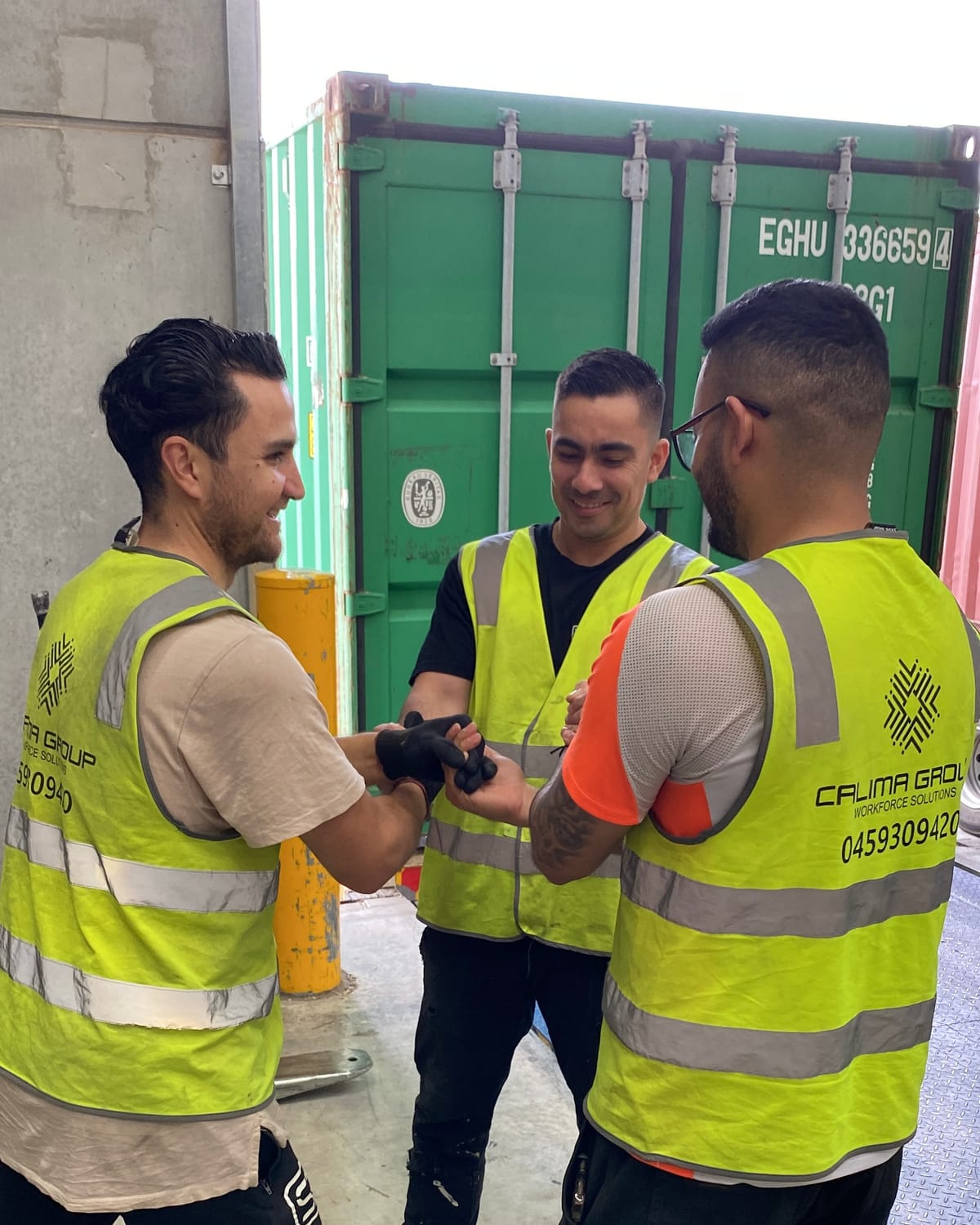 Three Calima workers in branded hi-vis sharing a fist bump on site